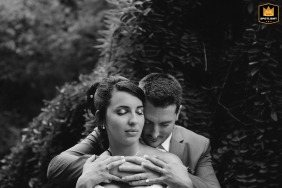 In the large park of Mondonville, the groom gently wraps his hands around the bride’s shoulders, creating an intimate, black-and-white symmetrical portrait of shared emotion.